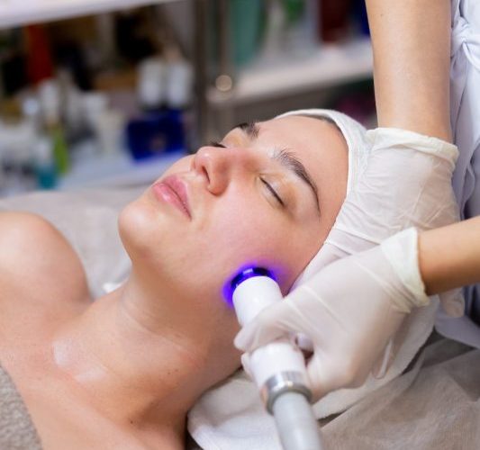 A young beautiful girl lies on the beautician's table and receives procedures with a professional apparatus for skin rejuvenation and moisturizing